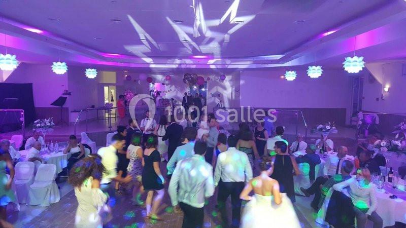 Des invités dansent dans une salle de réception éclairée par des lumières colorées lors d'une fête.