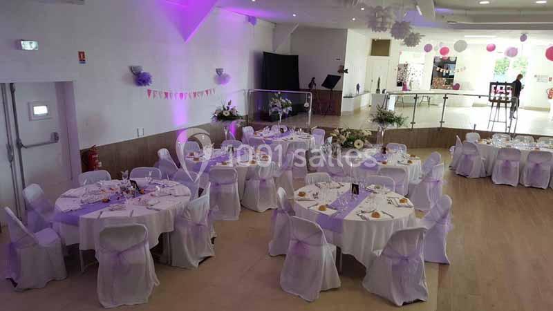 Salle de réception décorée avec des tables rondes dressées, nappes blanches et éclairage violet.