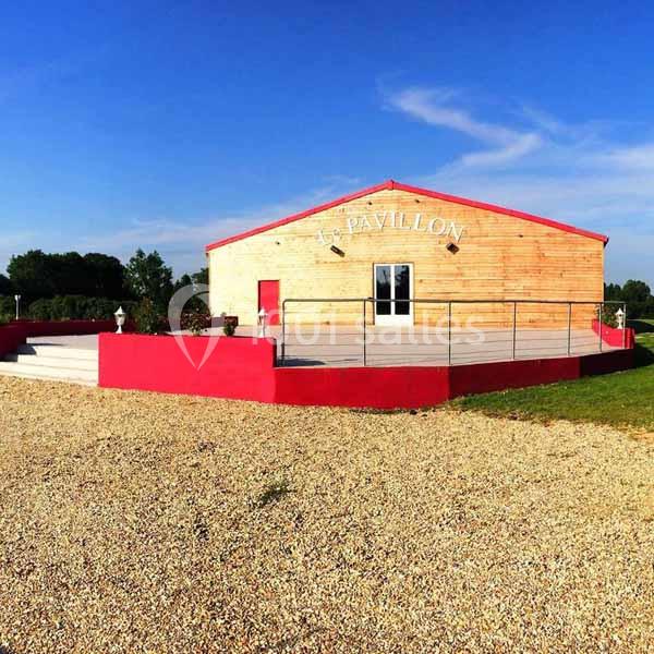 Bâtiment en bois avec terrasse surélevée, façade rouge et inscription ’Pavillon’, entouré d'un espace gravillonné.