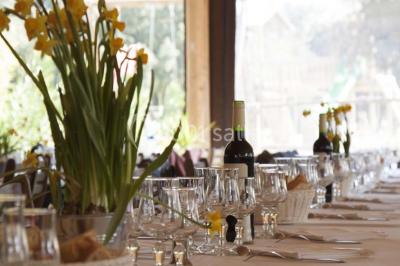 Table et chaises en métal noir installées sous des arbres, près d'une grande fenêtre reflétant l'extérieur.