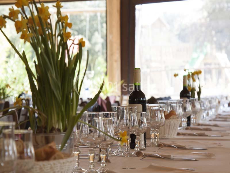 Table dressée avec des verres, couverts, bouteilles de vin et décorations florales jaunes dans une salle lumineuse.