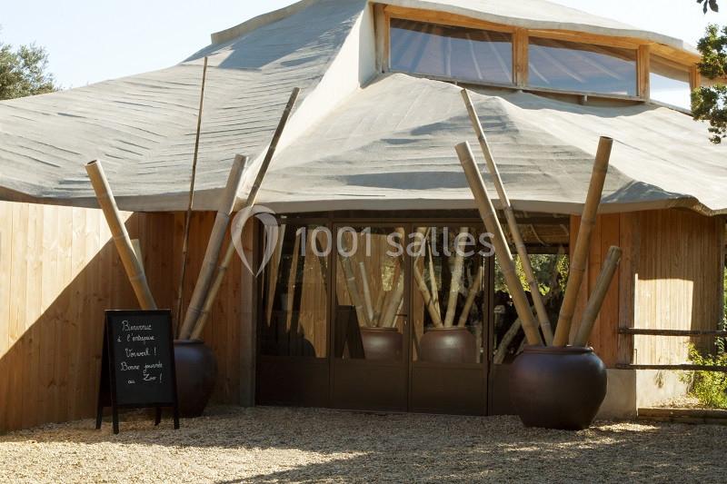 Entrée d’un bâtiment en bois avec une structure originale et des pots contenant de grands bambous.