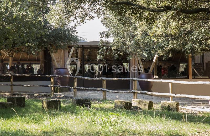 Un bâtiment en bois entouré d'arbres, avec une clôture en premier plan et des visiteurs à l'intérieur.