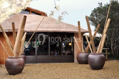 Table et chaises en métal noir installées sous des arbres, près d'une grande fenêtre reflétant l'extérieur.