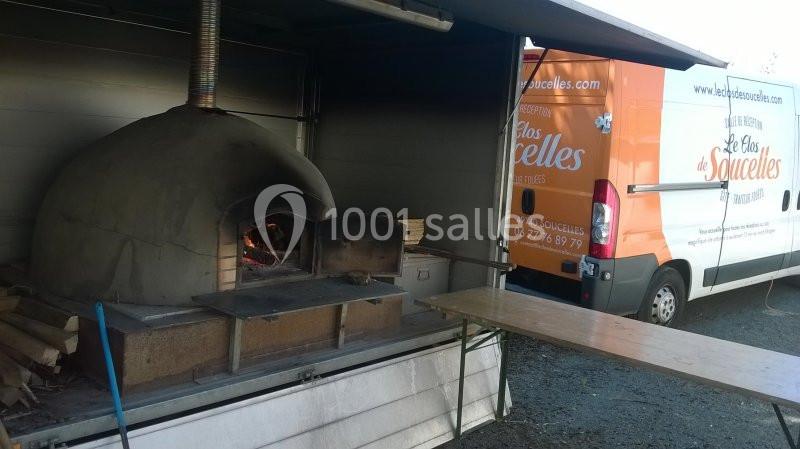 Four à bois en extérieur avec des bûches à proximité, installé près d'un camion utilitaire ouvert.