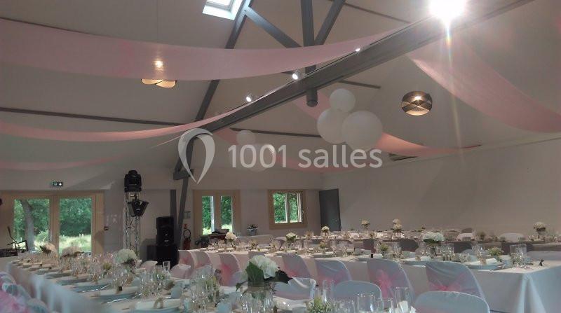 Salle de réception décorée avec des tables dressées, des nappes blanches, des fleurs et des voilages roses suspendus.