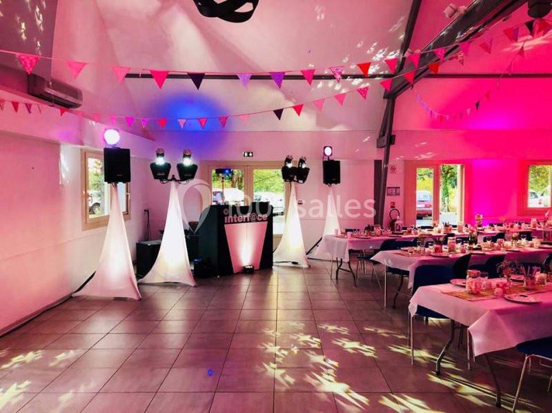 Salle décorée pour un événement, avec guirlandes colorées, tables dressées et éclairage rose.