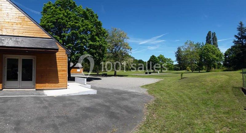 Bâtiment en bois avec porte vitrée, entouré d'une pelouse, d'arbres et d'un ciel dégagé.