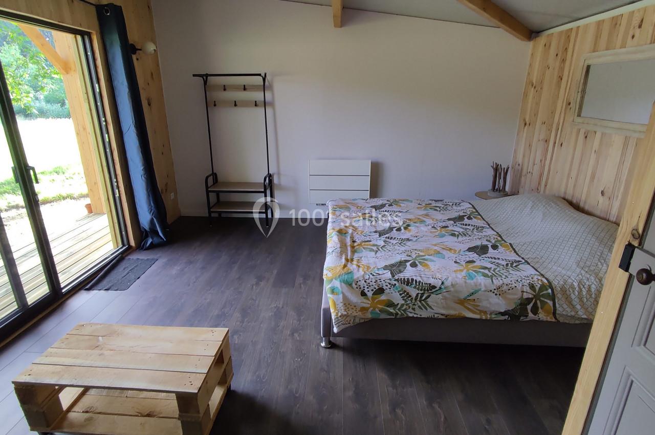 Chambre lumineuse avec parquet sombre, lit double, table basse en bois et porte-fenêtre donnant sur l'extérieur.