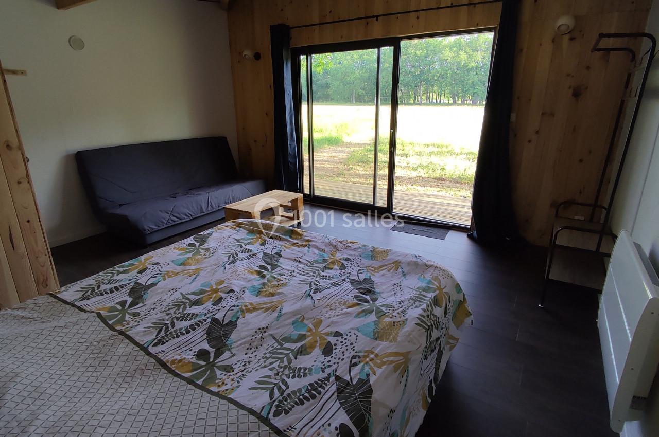 Chambre avec lit double, canapé, table basse et grande baie vitrée donnant sur un paysage de prairie et forêt.