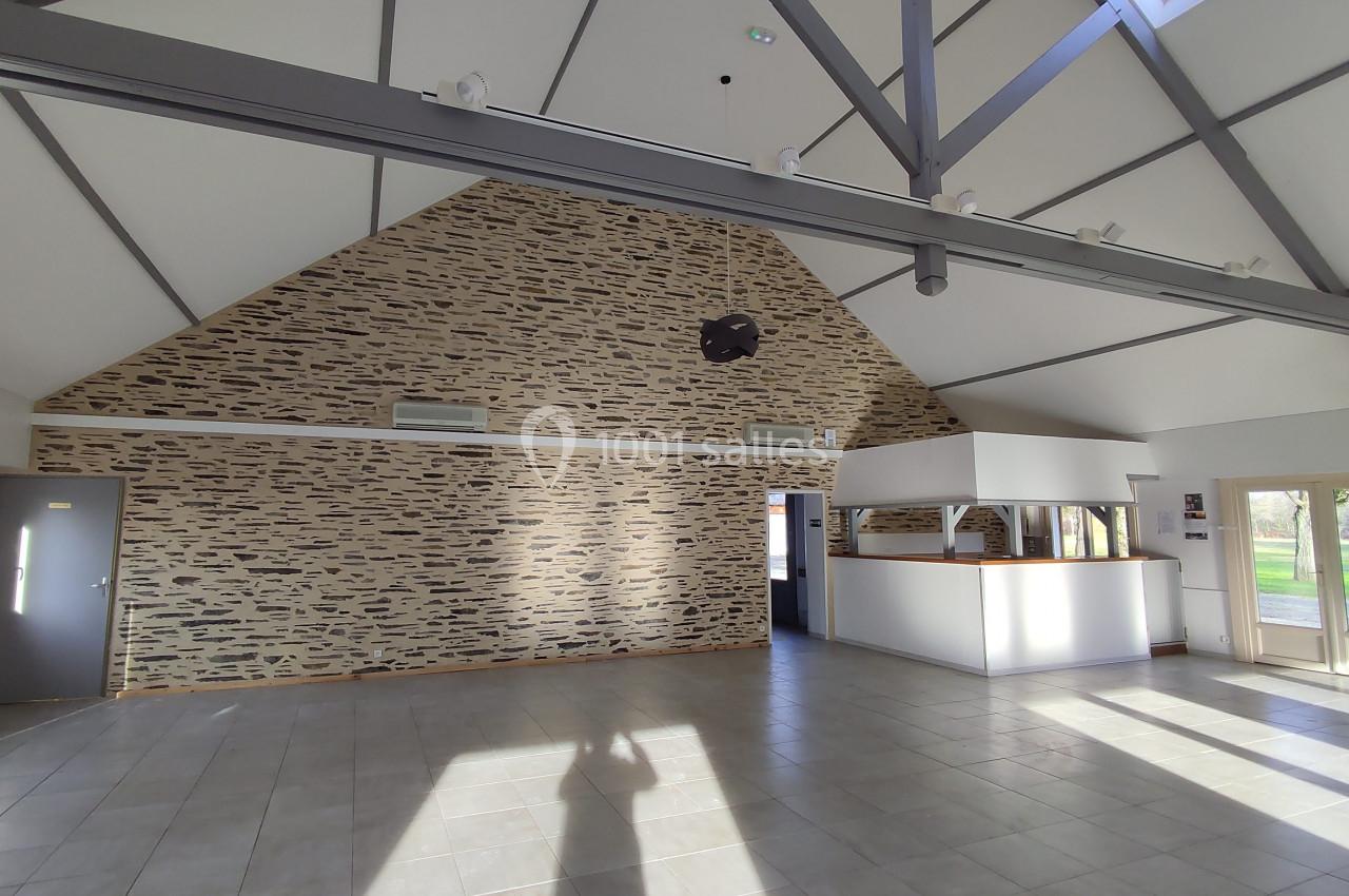 Salle lumineuse avec murs en pierre apparente, plafond haut avec poutres métalliques et carrelage au sol.