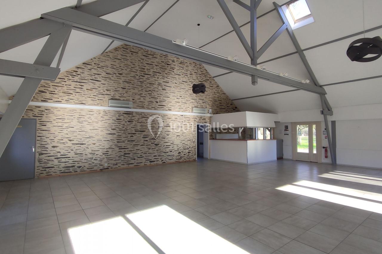 Salle lumineuse avec murs en pierre, poutres apparentes, carrelage au sol et comptoir blanc près d'une fenêtre.