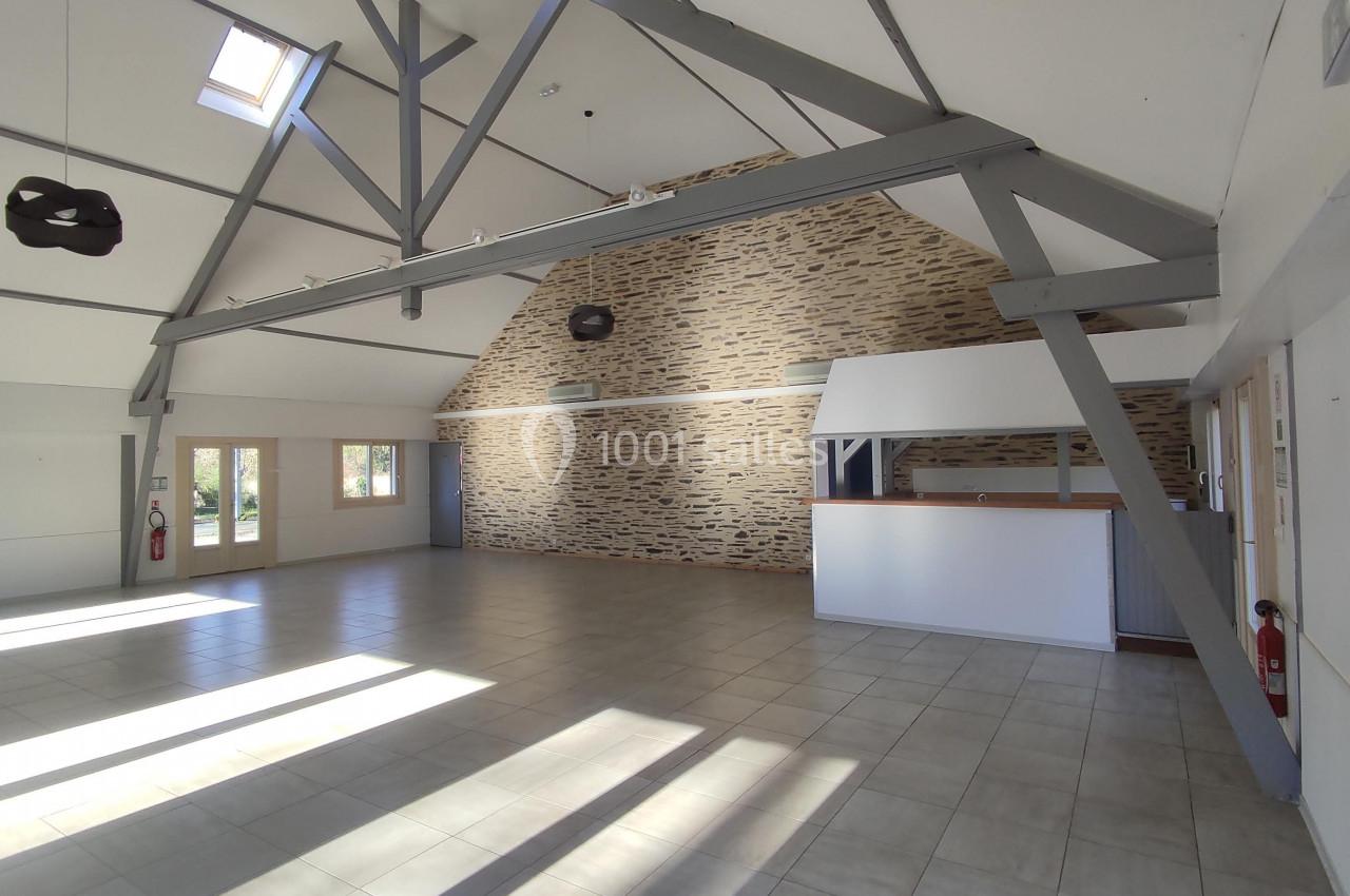 Salle lumineuse avec murs en pierre, poutres apparentes, carrelage au sol et un comptoir en bois clair.