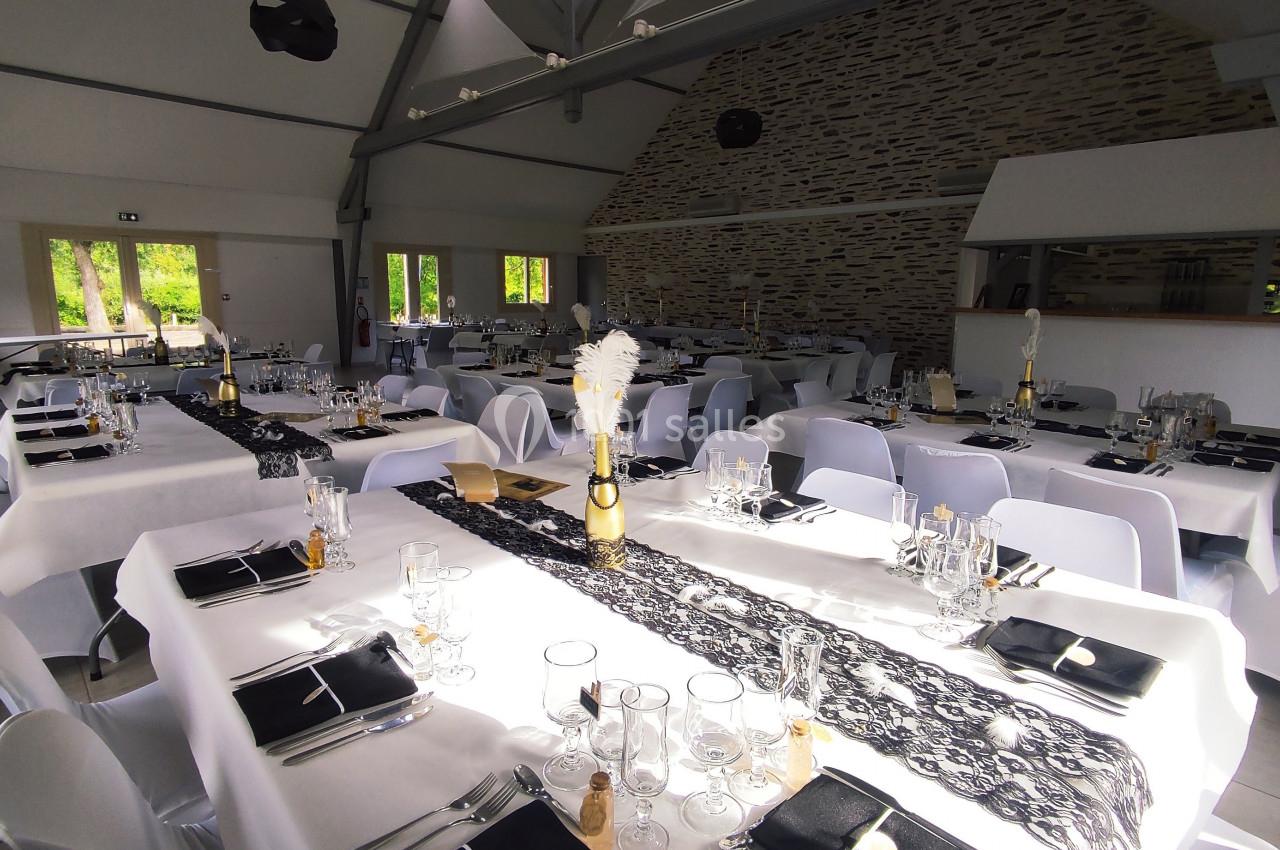 Salle de réception décorée avec des tables dressées, nappes blanches et chemins de table noirs en dentelle.