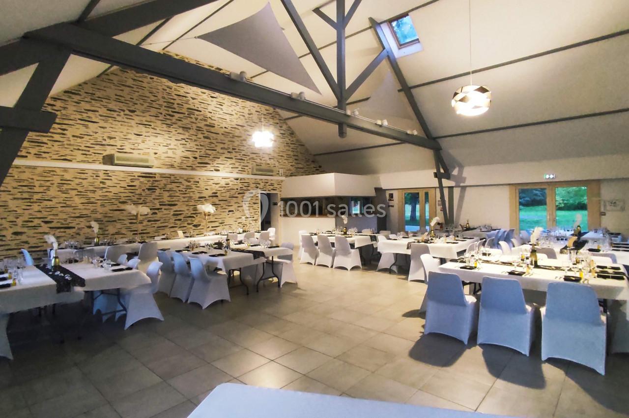 Salle de réception spacieuse avec tables dressées, chaises blanches et murs en pierre apparente.