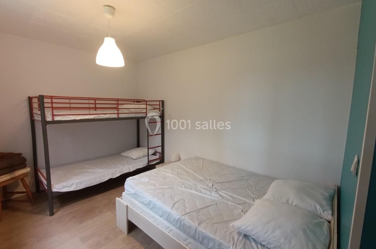 Chambre avec un lit double, un lit superposé, murs blancs, sol en bois clair et lampe suspendue.