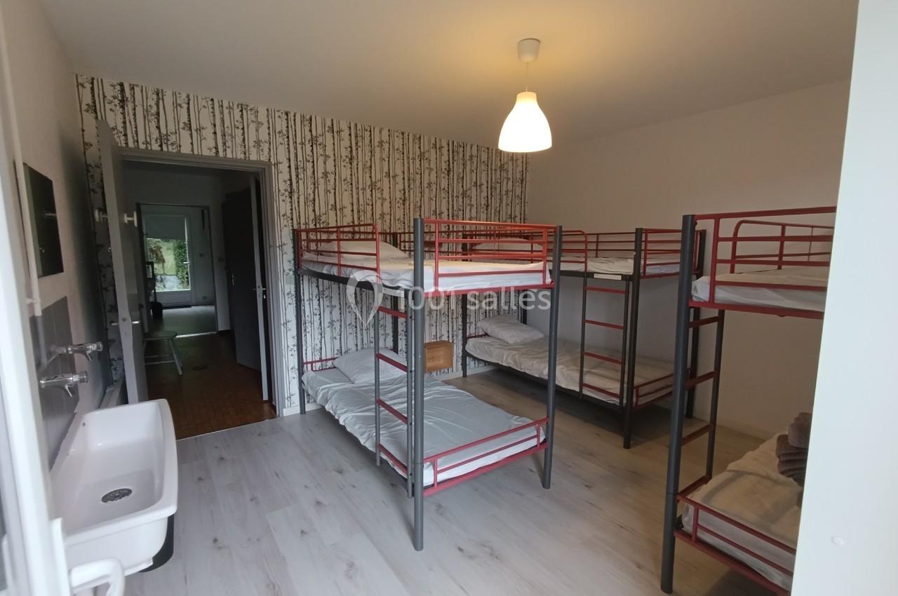 Dortoir avec lits superposés en métal, lavabo, parquet clair et papier peint à motif de bouleaux.