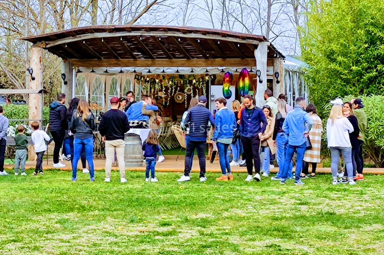 Des personnes font la queue devant un stand en plein air proposant des articles colorés, entouré de verdure.