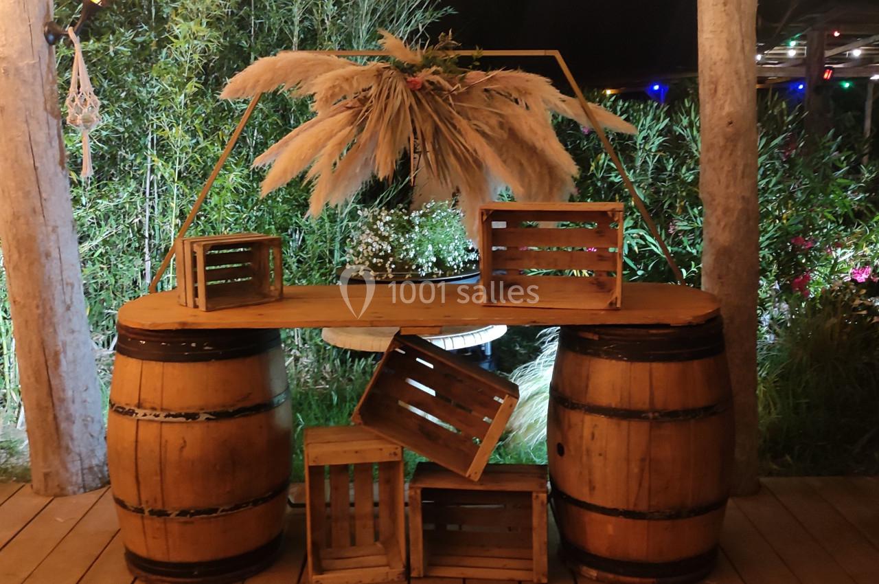 Deux tonneaux en bois soutenant une planche décorée de caisses en bois, de fleurs et de pampas, en extérieur nocturne.