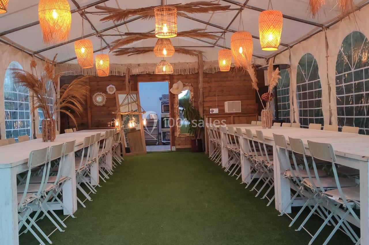 Intérieur d'une tente aménagée avec de longues tables blanches, des chaises pliantes et des lampes suspendues.