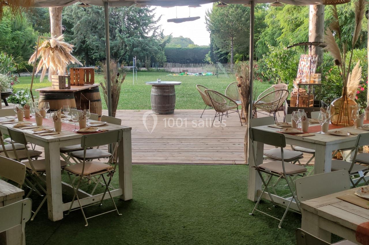 Salle de réception en plein air avec tables dressées, vue sur un jardin verdoyant et une terrasse en bois.