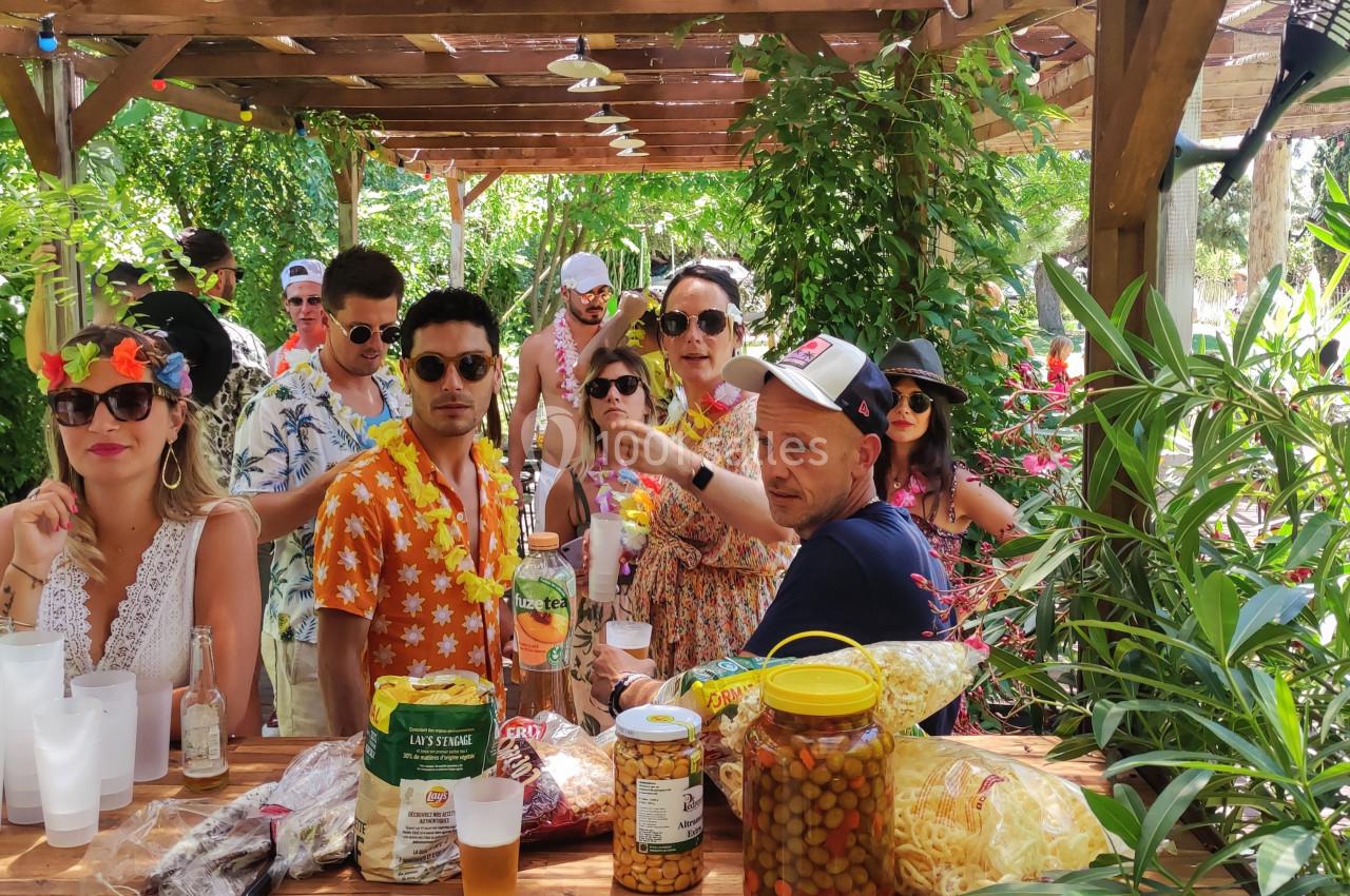 Groupe de personnes en tenue estivale réunies autour d'un bar en bois, entouré de végétation luxuriante.