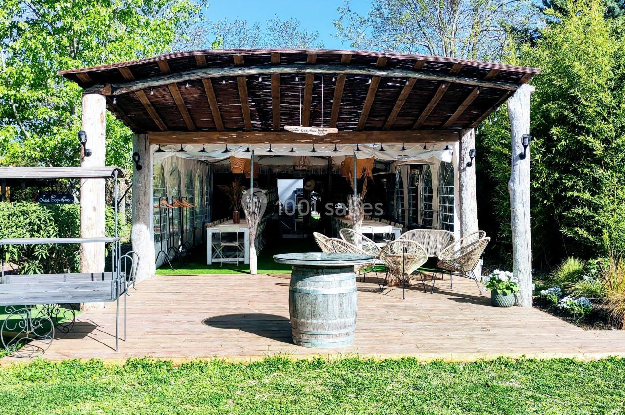 Terrasse en bois avec mobilier de jardin, abri en bois et verdure environnante sous un ciel ensoleillé.