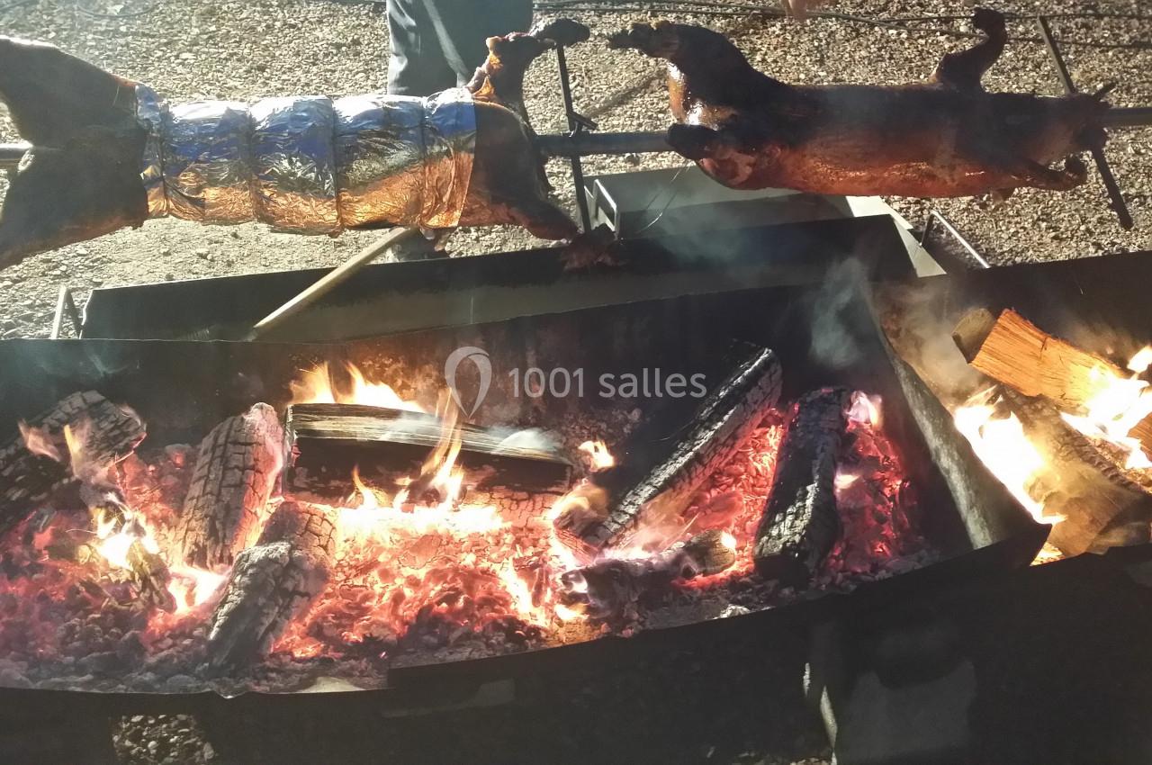Deux animaux entiers rôtissent sur des broches au-dessus d'un feu de bois avec des braises incandescentes.