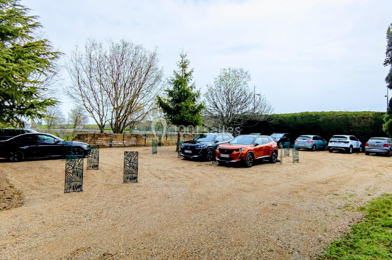 Plusieurs voitures garées sur un parking en gravier entouré d'arbres et de végétation.