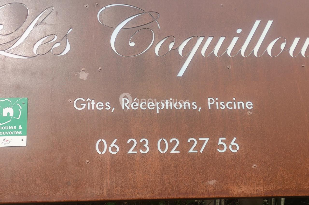 Panneau en métal rouillé indiquant ’Les Coquilloux’, avec des informations sur des gîtes, réceptions, piscine et un numéro…