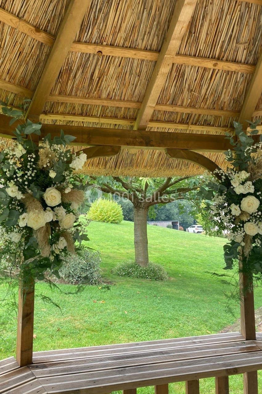 Deux arrangements floraux blancs et verts décorent une pergola en bois avec vue sur un jardin verdoyant.