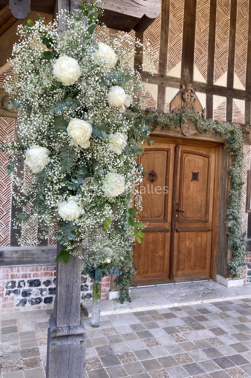 Décoration florale avec pivoines blanches et gypsophile suspendue près d'une porte en bois dans un cadre rustique.