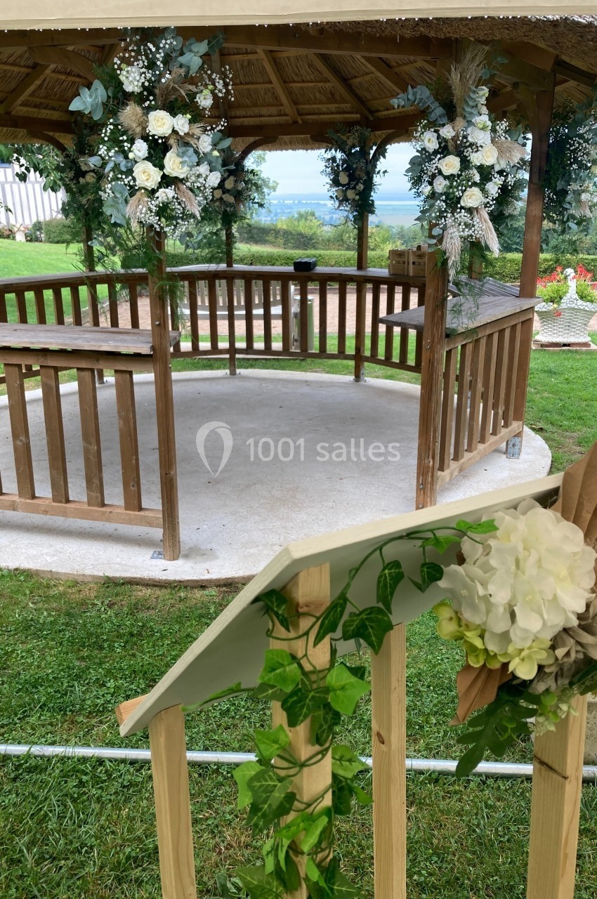 Kiosque en bois décoré de fleurs blanches et feuillages, situé dans un jardin verdoyant.