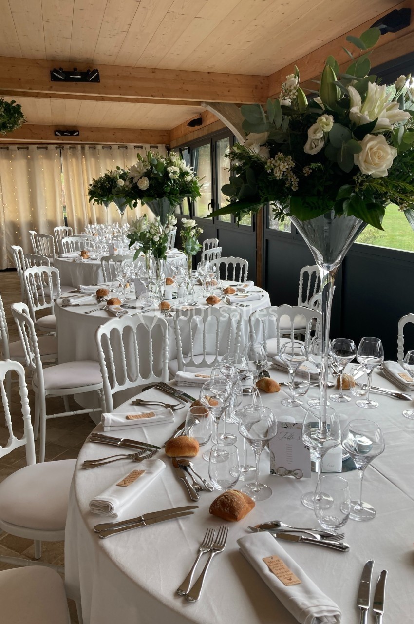 Salle de réception décorée avec des tables rondes dressées, nappes blanches, couverts élégants et centres de table floraux.