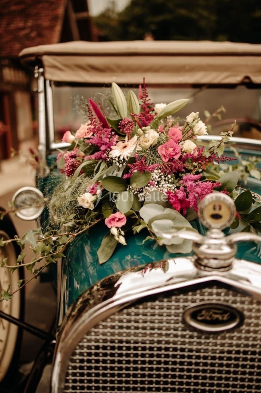 Arrangement floral coloré sur le capot d'une voiture ancienne verte avec une calandre en métal.
