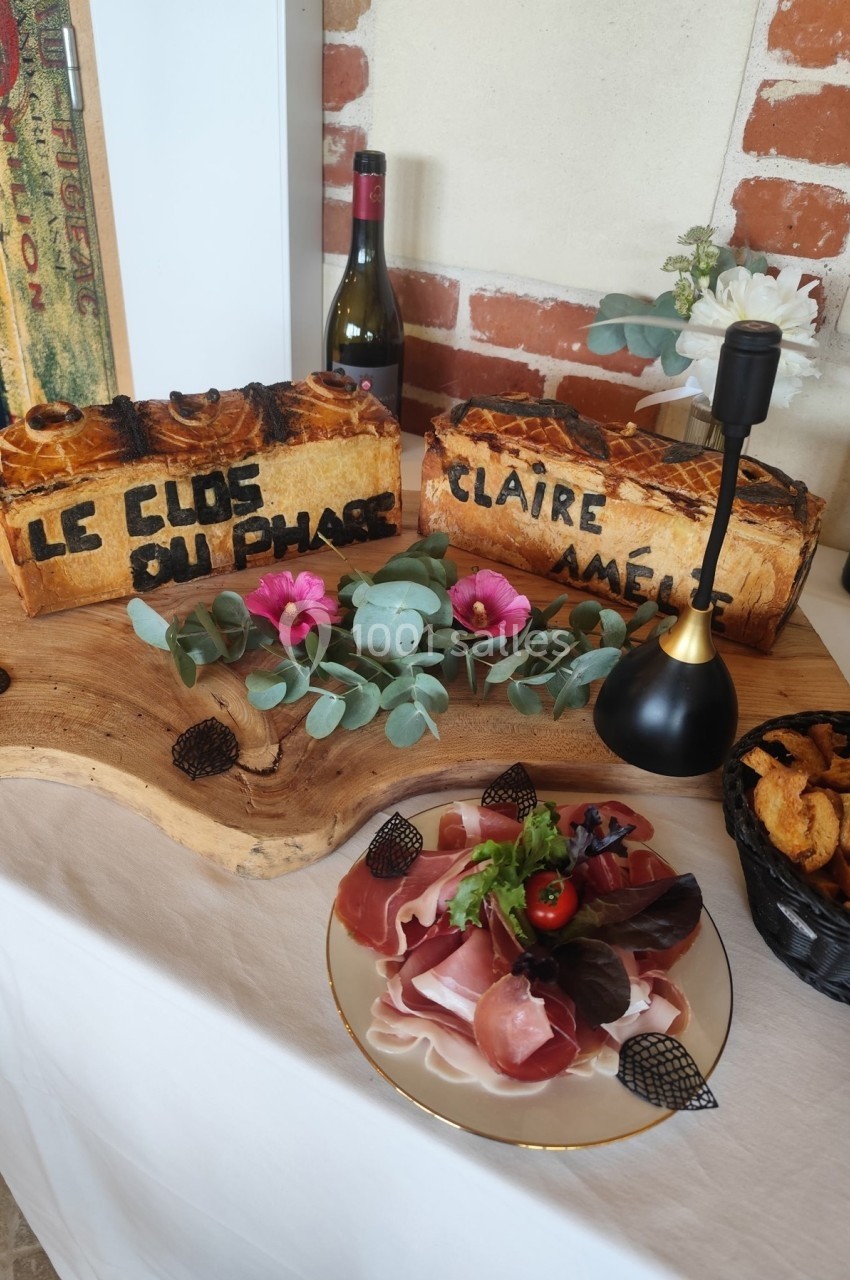 Plateau avec pains personnalisés, charcuterie, salade, fleurs décoratives et bouteille de vin sur une table en bois.