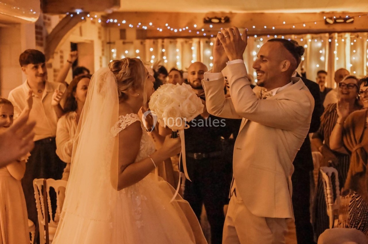 Un couple de mariés souriants danse entouré d'invités dans une salle décorée de guirlandes lumineuses.
