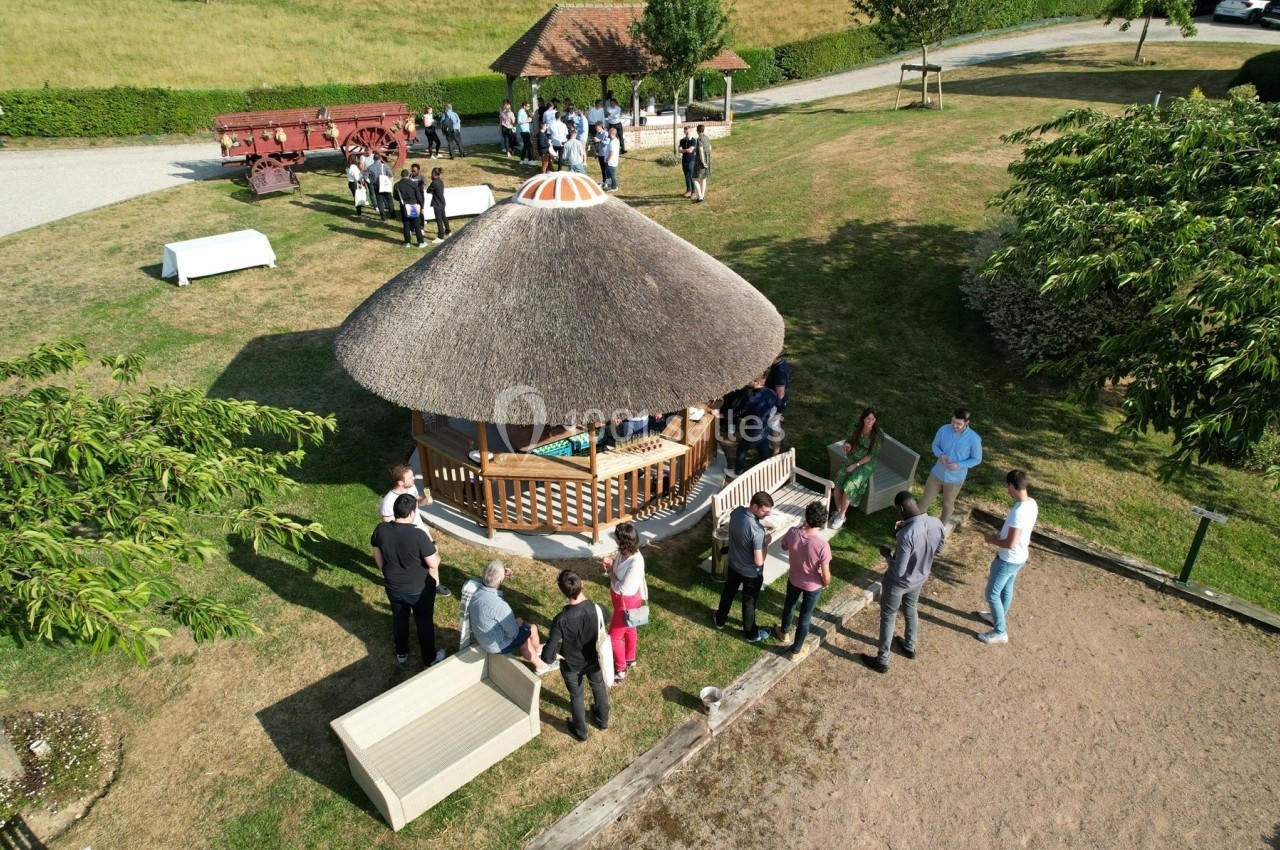 Groupe de personnes rassemblées autour d'une structure en bois avec toit en chaume dans un espace extérieur verdoyant.