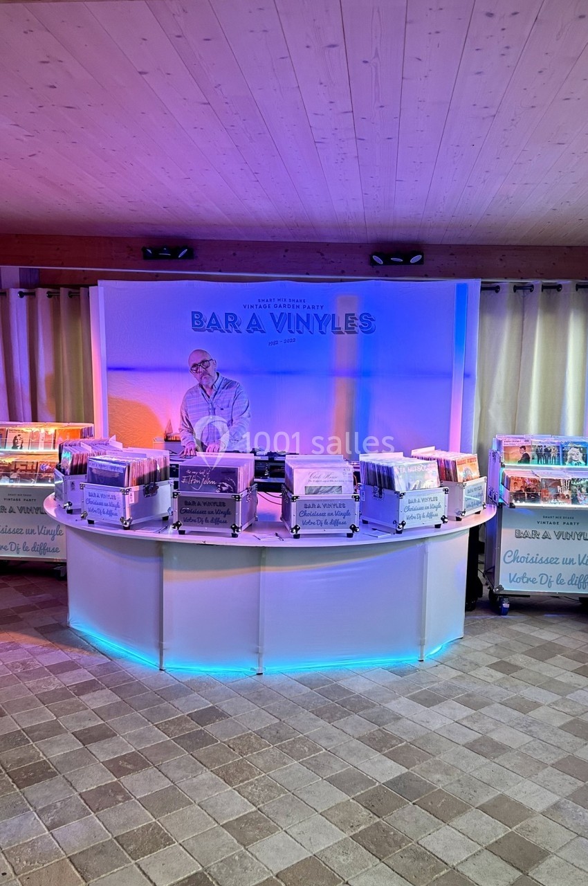 Stand circulaire de vente de vinyles avec un vendeur, éclairé par des lumières colorées dans un espace intérieur.