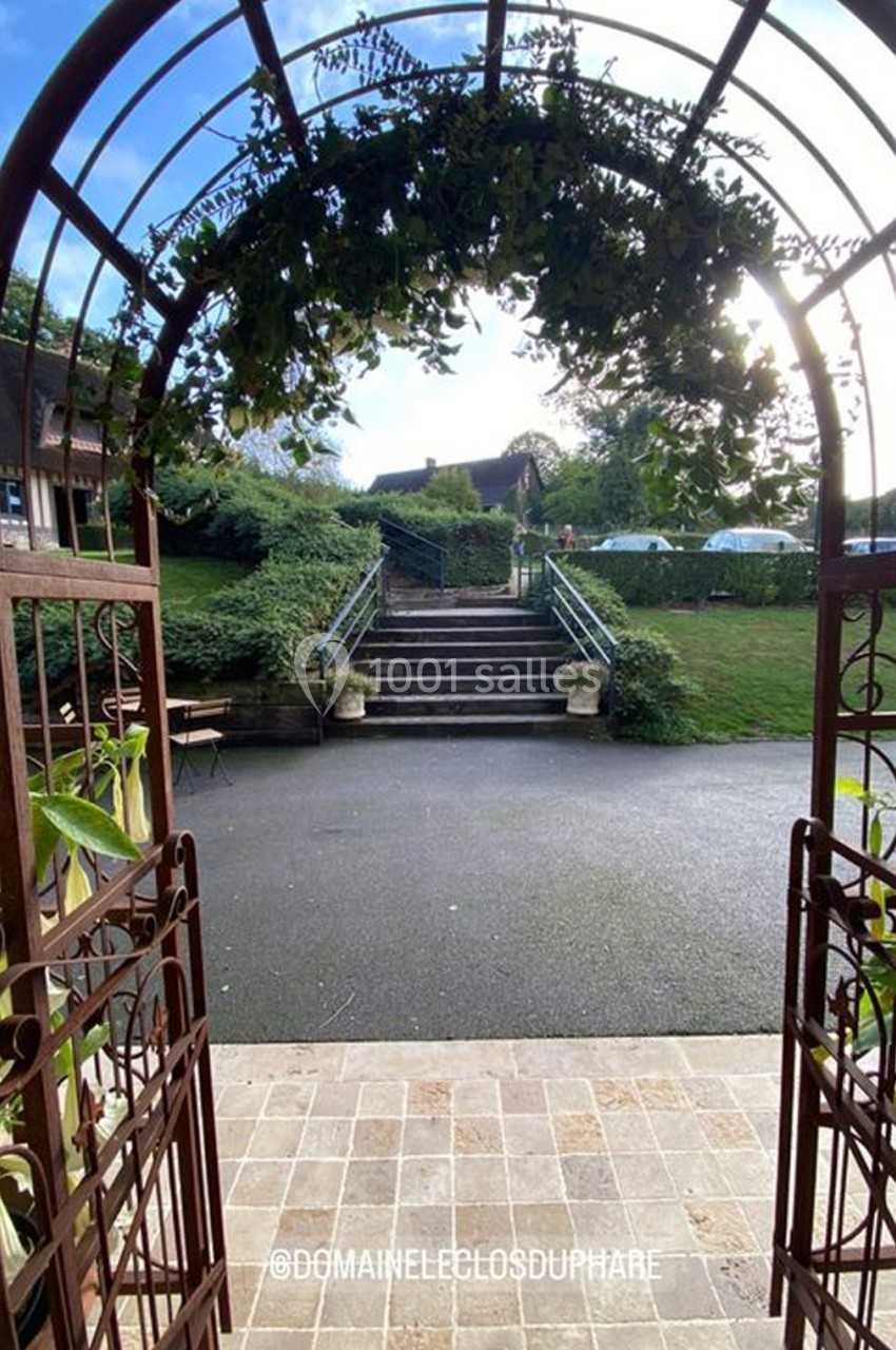Vue d'une arche en métal ornée de feuillage, donnant sur un chemin menant à un escalier et un jardin verdoyant.
