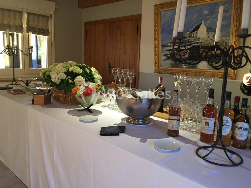 Table dressée avec des boissons, des verres, un seau à champagne, un panier de fleurs et des chandeliers dans une salle…