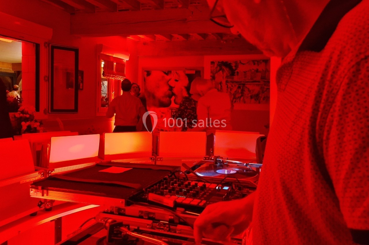 Un DJ mixe des vinyles dans une pièce éclairée de lumière rouge, avec des personnes en arrière-plan.