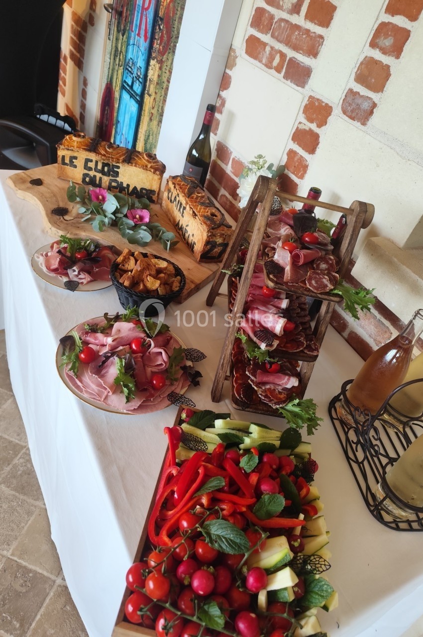 Buffet composé de charcuteries, légumes frais, pain et bouteilles de vin, disposé sur une table blanche.