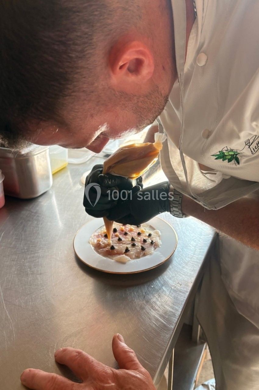 Un chef pâtissier décore un dessert avec une poche à douille sur un plan de travail en acier inoxydable.