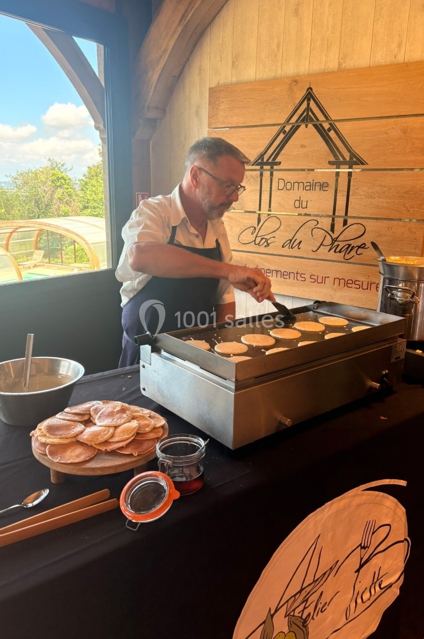 Un cuisinier prépare des crêpes sur une plaque chauffante lors d'un événement dans un cadre en bois lumineux.