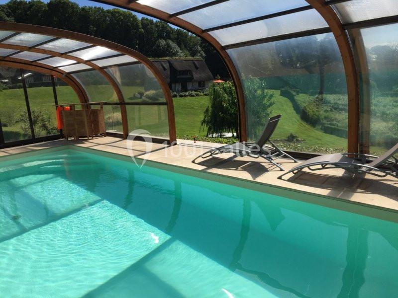 Piscine couverte avec structure en verre et bois, entourée de transats, donnant sur un jardin verdoyant.