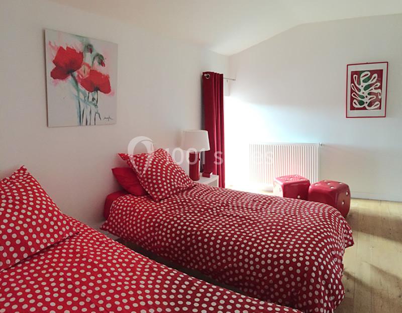 Deux lits simples avec housses rouges à pois blancs dans une chambre lumineuse décorée de touches rouges et blanches.