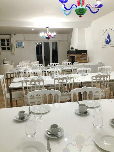 Salle à manger lumineuse avec tables dressées, chaises blanches et lustres colorés, donnant sur une baie vitrée.