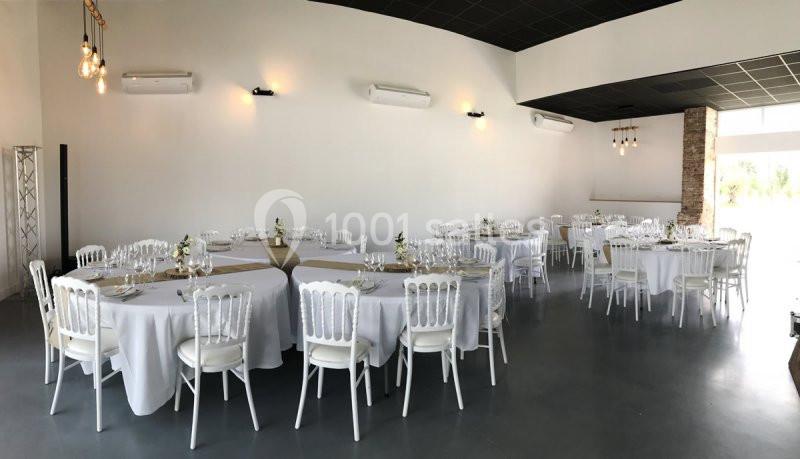 Salle de réception lumineuse avec tables rondes dressées, nappes blanches et chaises élégantes en plastique blanc.