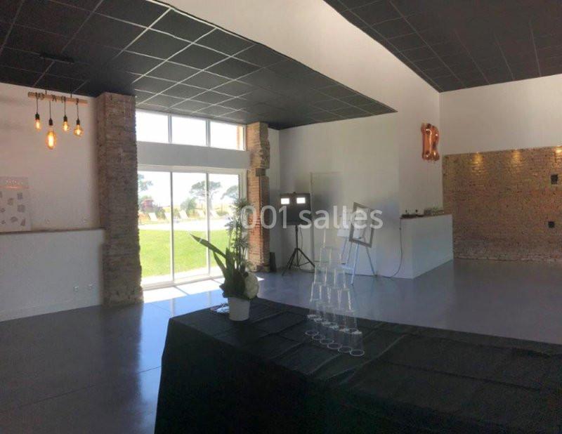 Salle lumineuse avec grandes baies vitrées, murs en briques, plafond noir et table décorée au premier plan.